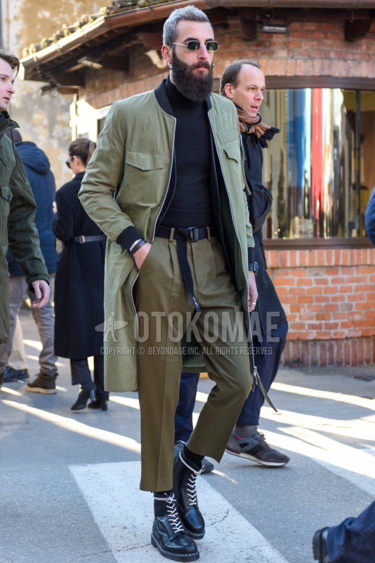 Men's fall/winter outfit with plain silver sunglasses, plain olive green outerwear, plain black turtleneck knit, plain black tape belt, plain beige chinos, plain beige pleated pants, plain beige cropped pants, and Dr. Martens black work boots Outfit.