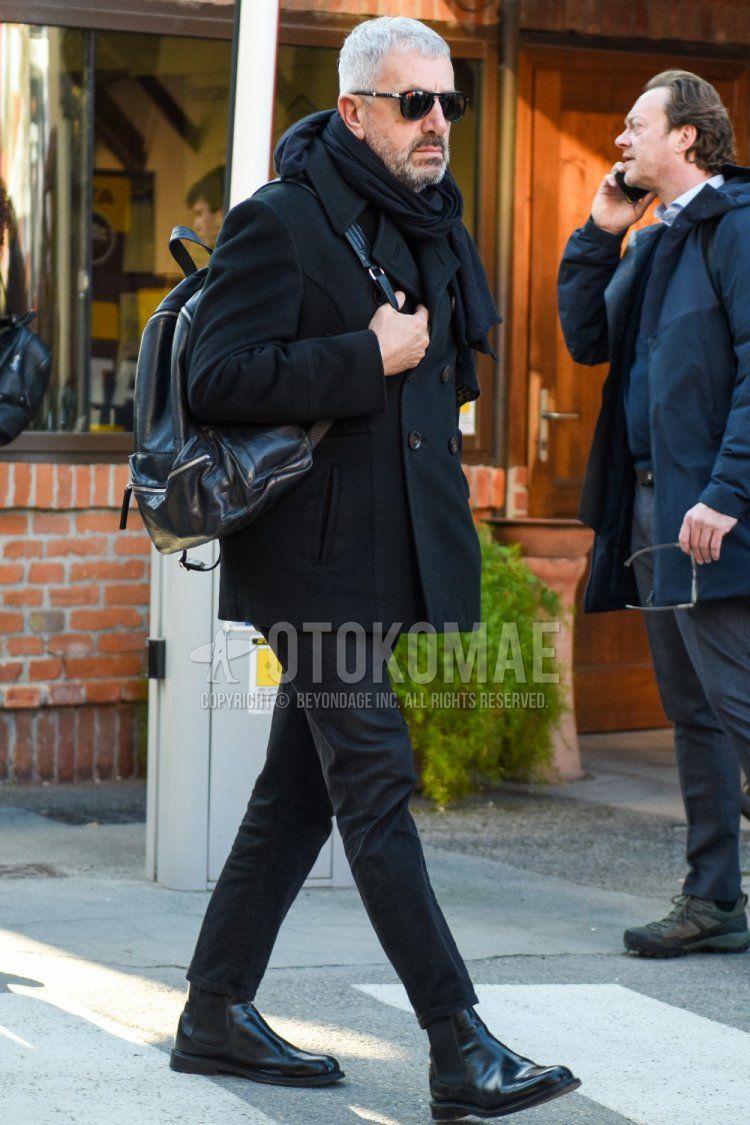 Men's fall/winter outfit with Persol solid black sunglasses, solid black scarf/stall, solid black P-coat, solid black cotton pants, solid black cropped pants, black side gore boots, and solid black backpack.