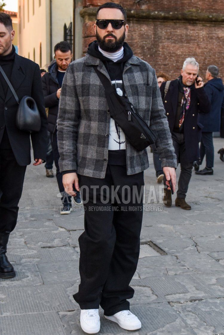 Men's fall/winter outfit with plain black sunglasses, gray checked shirt jacket, black graphic hoodie, plain white turtleneck knit, plain black cotton pants, Nike Air Force 1 white low-cut sneakers, plain black Prada shoulder bag.