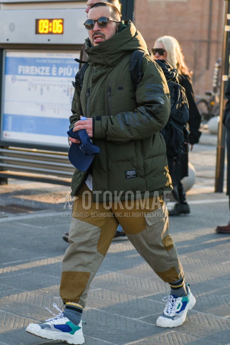 Winter men's coordinate and outfit with solid black sunglasses, solid olive green down jacket, solid beige chinos, solid beige cargo pants, solid beige jogger pants/ribbed pants, solid gray socks, and white low-cut sneakers.