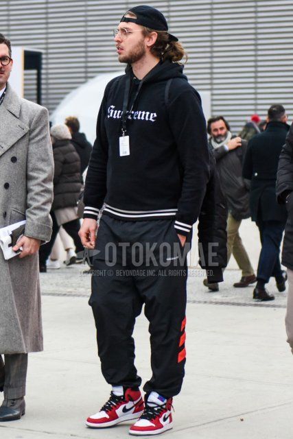 Spring and fall men's coordinate and outfit with plain black baseball cap, plain silver glasses, Supreme black decal logo hoodie, Adidas plain black jogger pants/ribbed pants, and Nike Air Jordan 1 Chicago red and white high-cut sneakers.