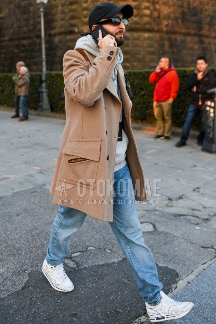 Men's fall/winter coordinate and outfit with solid black baseball cap, solid black sunglasses, solid beige chester coat, solid gray hoodie, solid light blue denim/jeans, and white low-cut Nike sneakers.