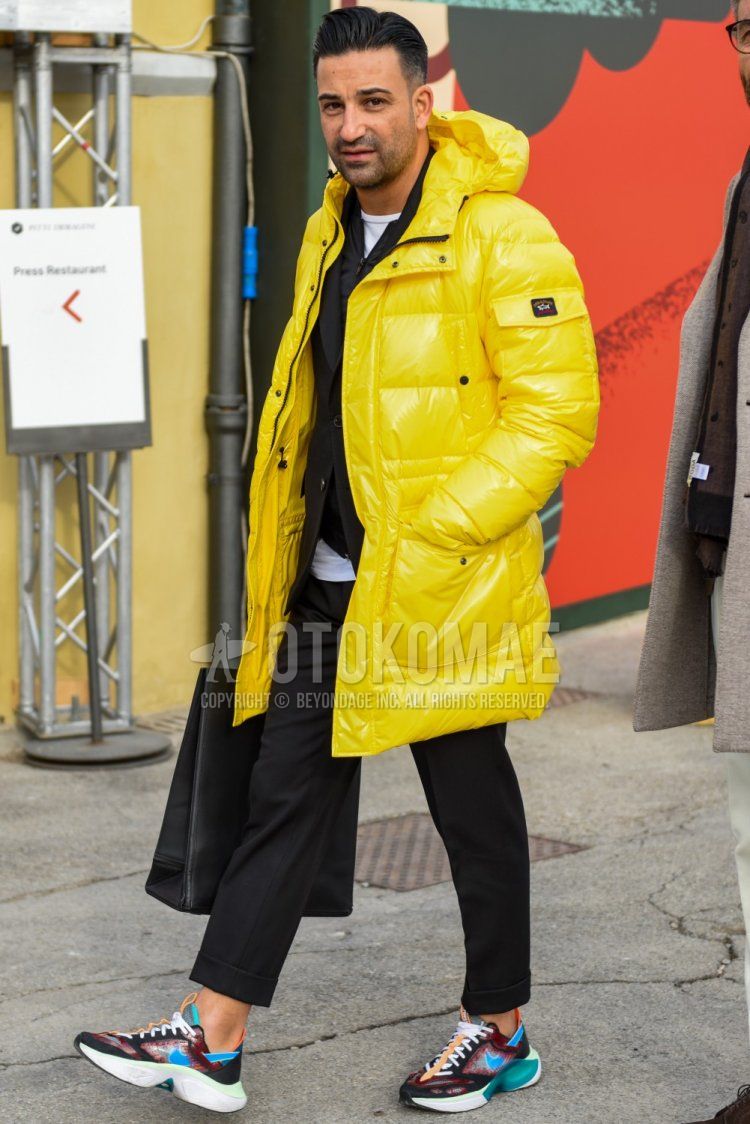 Winter men's coordinate and outfit with a solid yellow hooded coat from Paul and Shark, solid yellow down jacket, solid black inner down, Nike multi-colored low-cut sneakers, and solid black suit.