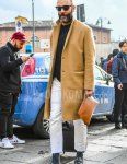 Men's fall/winter outfit with solid black sunglasses, solid beige chester coat, solid black sweater, solid white denim/jeans, solid gray socks, Gucci black bit loafer leather shoes, solid brown clutch/second bag/drawler.