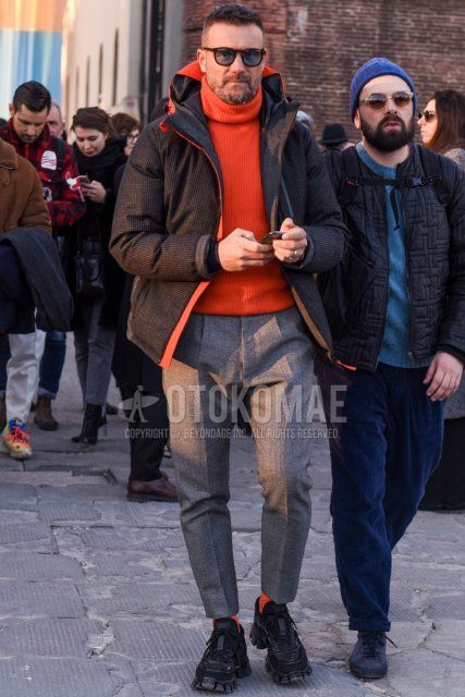 Men's winter outfit with brown tortoiseshell sunglasses, black checked down jacket, solid orange turtleneck knit, solid gray slacks, solid gray ankle pants, solid gray pleated pants, solid orange socks, black low-cut Prada sneakers How to wear.