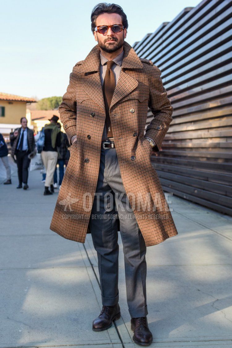 Men's fall/winter outfit with brown tortoiseshell sunglasses, brown checked trench coat, plain brown shirt, plain brown leather belt, plain gray slacks, brown plain toe leather shoes, and plain beige tie.