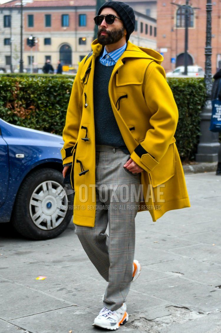 Men's fall/winter outfit with plain black sunglasses, plain yellow duffle coat, blue striped shirt, plain gray sweater, gray checked slacks, Balenciaga track trainers with white low-cut sneakers.