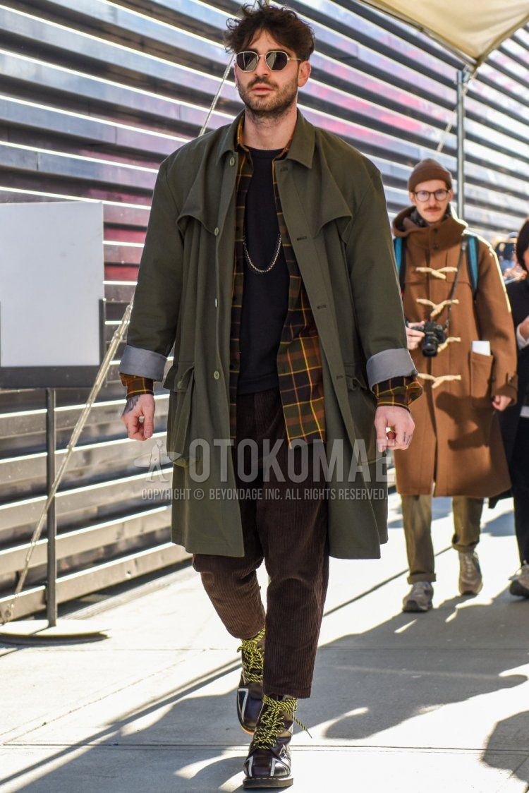 Silver solid sunglasses, olive green solid trench coat, multi-colored checked shirt, black solid t-shirt, brown solid cropped pants, brown solid winter pants (corduroy, velour), Dr. Martens brown work boots for fall and winter. Men's coordinate/outfit.