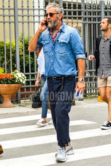 Men's spring/summer/fall outfit with brown tortoiseshell sunglasses, solid light blue denim/chambray shirt, solid gray t-shirt, black leather belt, solid navy chinos, and gray low-cut Nike Air Harachi sneakers.