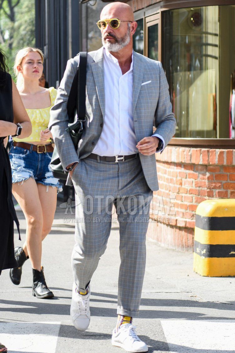 Men's spring, summer, and fall coordination and outfit with plain yellow sunglasses, plain light blue shirt, plain black leather belt from Hermes, plain yellow socks, white low-cut sneakers, and gray checked suit.