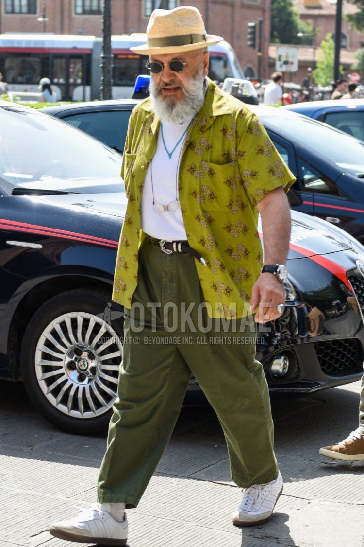 Men's spring/summer/fall outfit with solid beige hat, solid gold/black sunglasses, green top/inner shirt, solid white t-shirt, solid brown leather belt, solid green wide-leg pants, and white low-cut sneakers.
