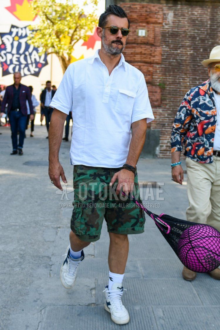 Men's summer coordinate and outfit with brown tortoiseshell sunglasses, plain white shirt, green camouflage cotton pants, plain white Diadora socks, and white high-cut Diadora sneakers.