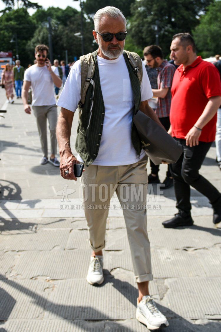 Men's spring/summer coordinate and outfit with plain black sunglasses, plain olive green gilet, plain white t-shirt, plain beige chinos, plain pleated pants, and white low-cut sneakers.