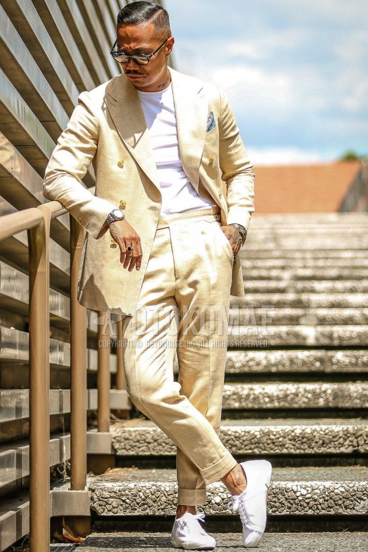Men's spring/summer coordination and outfit with plain black sunglasses, plain white T-shirt, white sneakers, and plain beige suit.