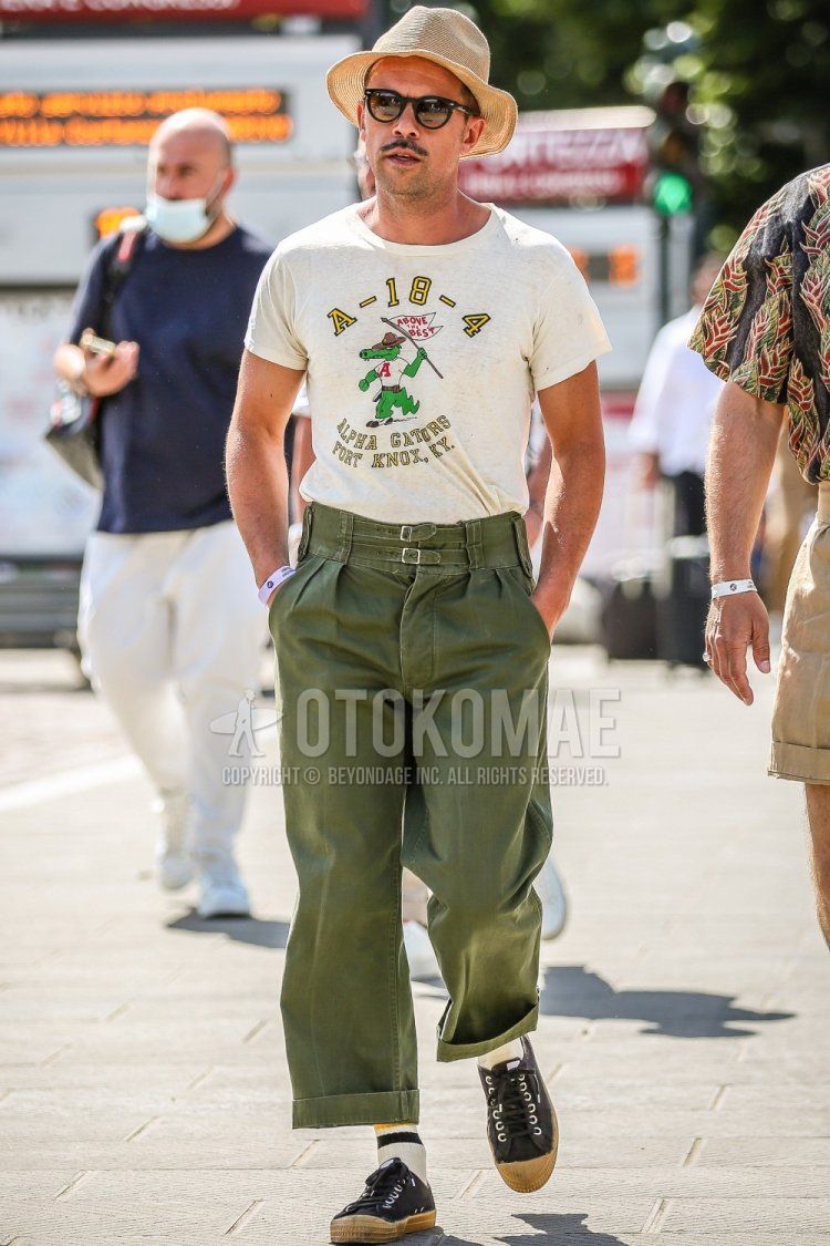 Men's spring/summer coordinate and outfit with plain brown/beige hat, plain black sunglasses, white graphic t-shirt, olive green plain wide-leg pants, white striped socks, and black sneakers.