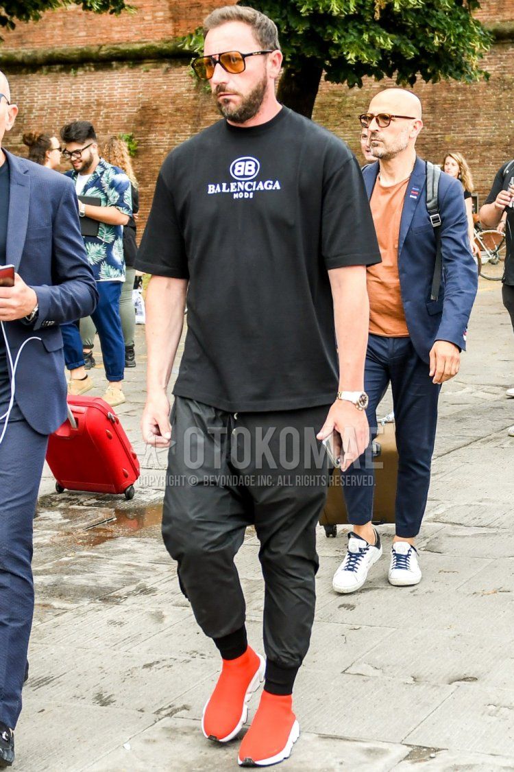 Men's spring/summer coordinate and outfit with plain black sunglasses, Balenciaga black deca logo t-shirt, plain black jogger pants/ribbed pants, and red high-cut sneakers with Balenciaga speed trainers.