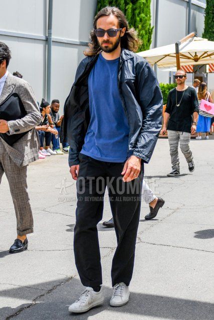 Men's spring, summer, and fall coordinate and outfit with solid color sunglasses, solid color black coach jacket, solid color blue t-shirt, solid color black cotton pants, and white low-cut sneakers.