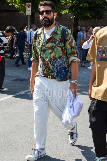 Spring and fall men's coordinate and outfit with square plain black sunglasses, green, brown and beige camouflage shirt jacket, plain white t-shirt, plain brown leather belt, plain white cotton pants and Converse All Star white low-cut sneakers.