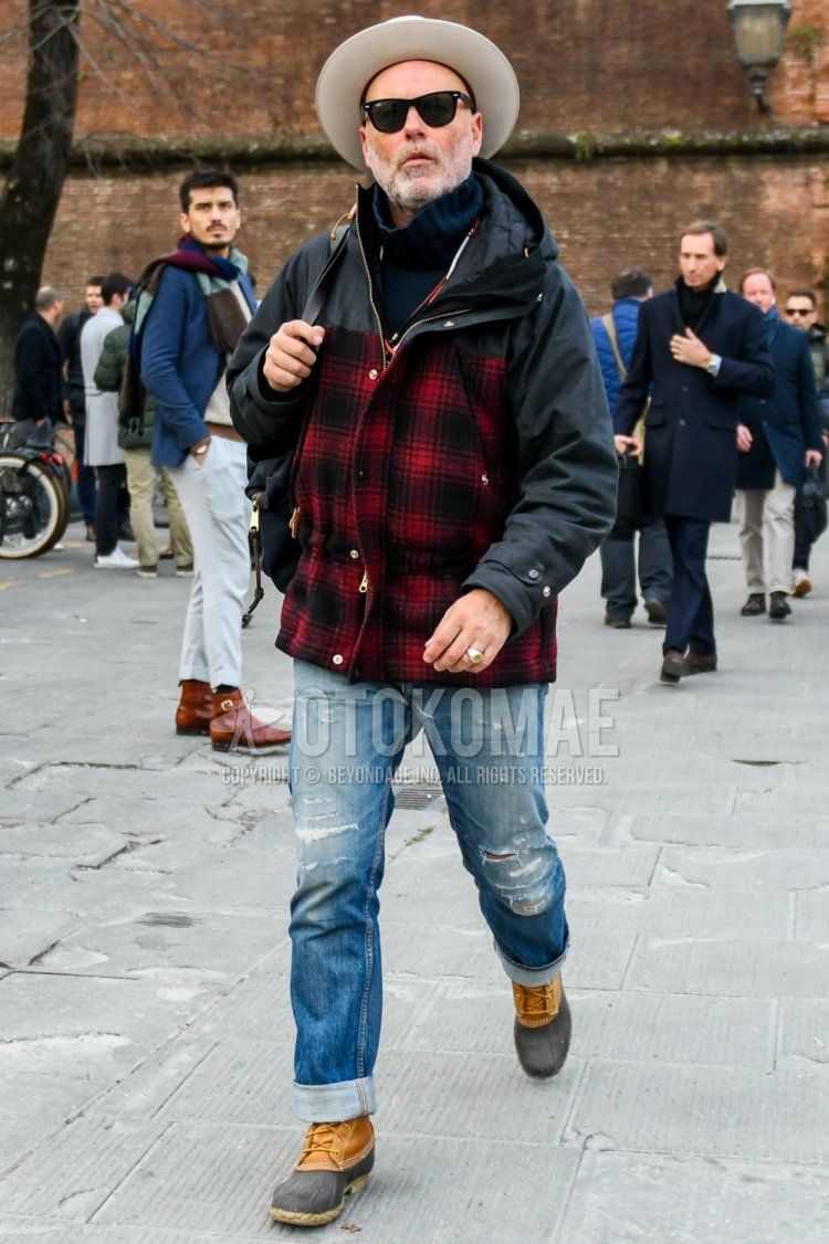 Men's fall/winter outfit with solid beige hat, solid sunglasses, solid black mountain parka, black/red checked mountain parka, solid navy turtleneck knit, solid blue denim/jeans, and gray/beige boots.