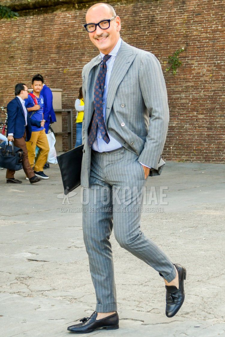 Men's spring/summer/autumn coordination and outfit with plain glasses, white/light blue striped shirt, black tassel loafer leather shoes, plain black clutch bag/second bag/drawstring, gray striped suit, and navy tie.