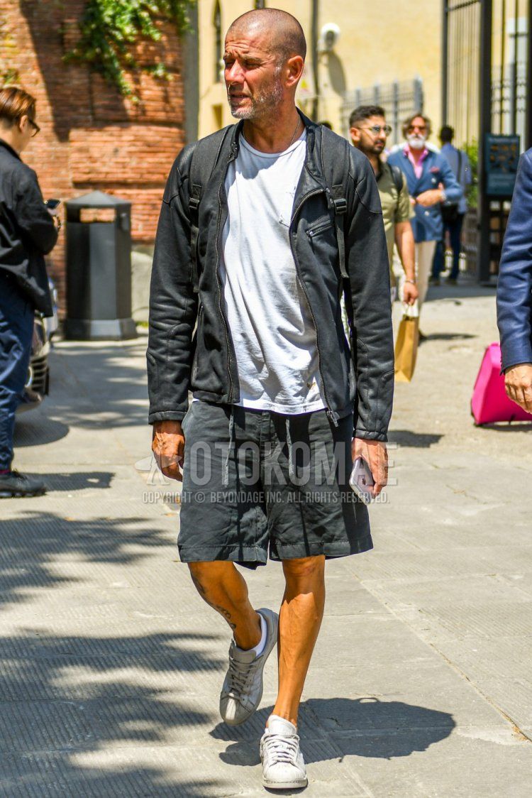 Men's spring and summer coordinate and outfit with plain black rider's jacket, plain white T-shirt, plain black shorts, and Adidas Superstar white low-cut sneakers.