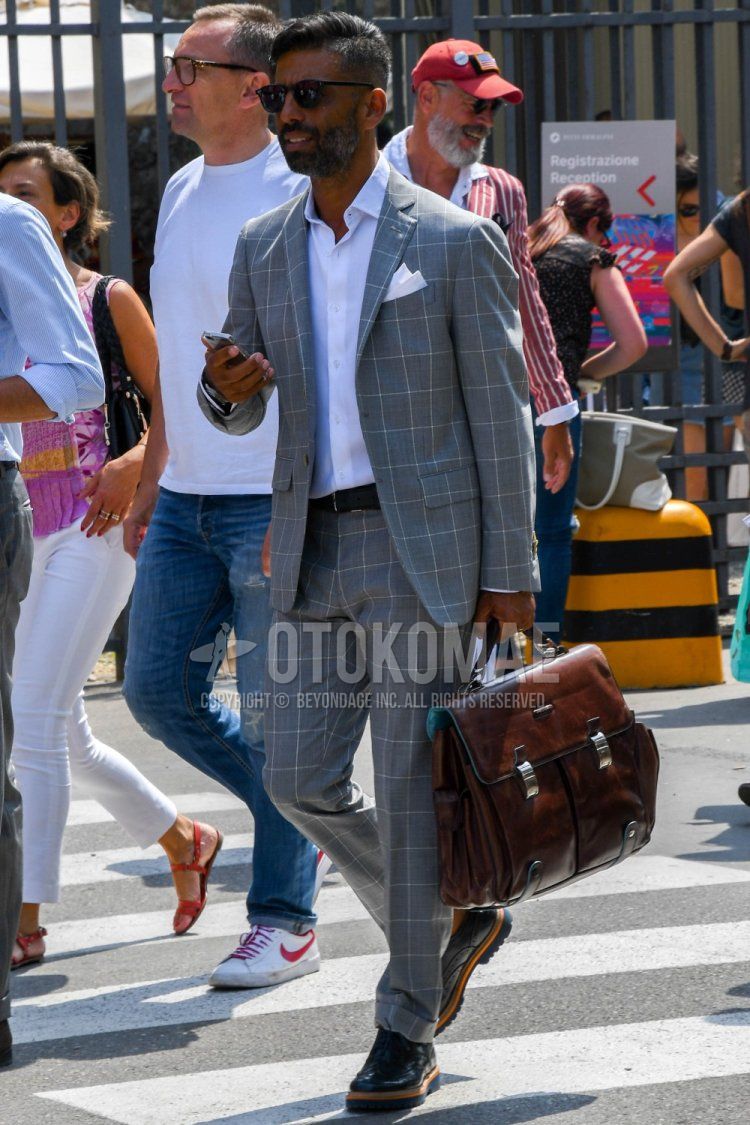 Men's spring/summer/fall outfit with plain black sunglasses from Boston, plain white shirt, plain black leather belt, black wingtip leather shoes, plain brown briefcase/handbag, and gray checked suit.