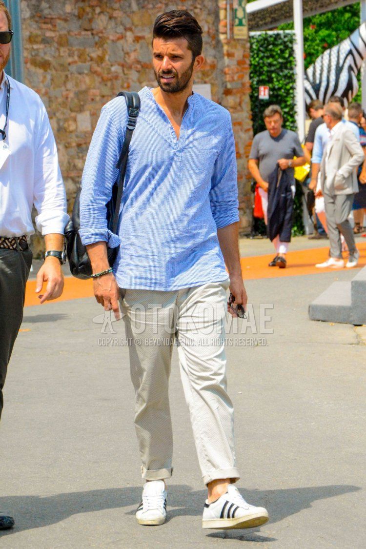 Men's spring and summer coordinate and outfit with pullover light blue striped shirt, beige dot chinos, Adidas Superstar white low-cut sneakers, and plain black backpack.