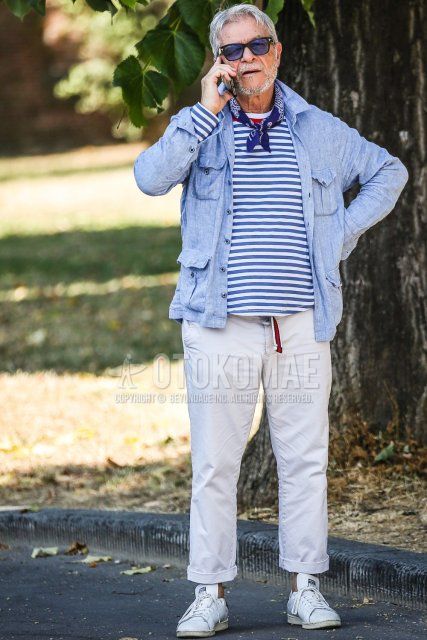 Men's spring/summer outfit with plain black Tom Ford sunglasses, blue/navy stole bandana/neckerchief, plain light blue shirt jacket, white/light blue striped t-shirt, red striped tape belt, plain beige ankle pants, and white Stan Smith sneakers. Outfit.