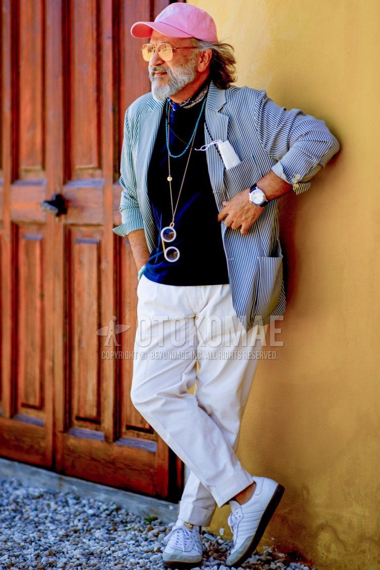 Men's spring/summer coordinate and outfit with plain pink baseball cap, plain yellow sunglasses, tailored jacket with blue graphics, plain black t-shirt, plain white cotton pants, and white sneakers.