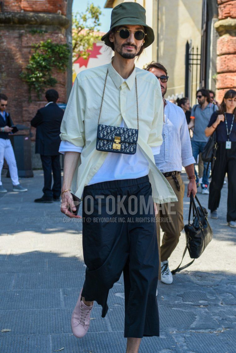 Summer men's coordinate and outfit with solid green hat, solid gold/black sunglasses, solid yellow shirt, solid white t-shirt, solid black cropped pants, and pink low-cut sneakers.