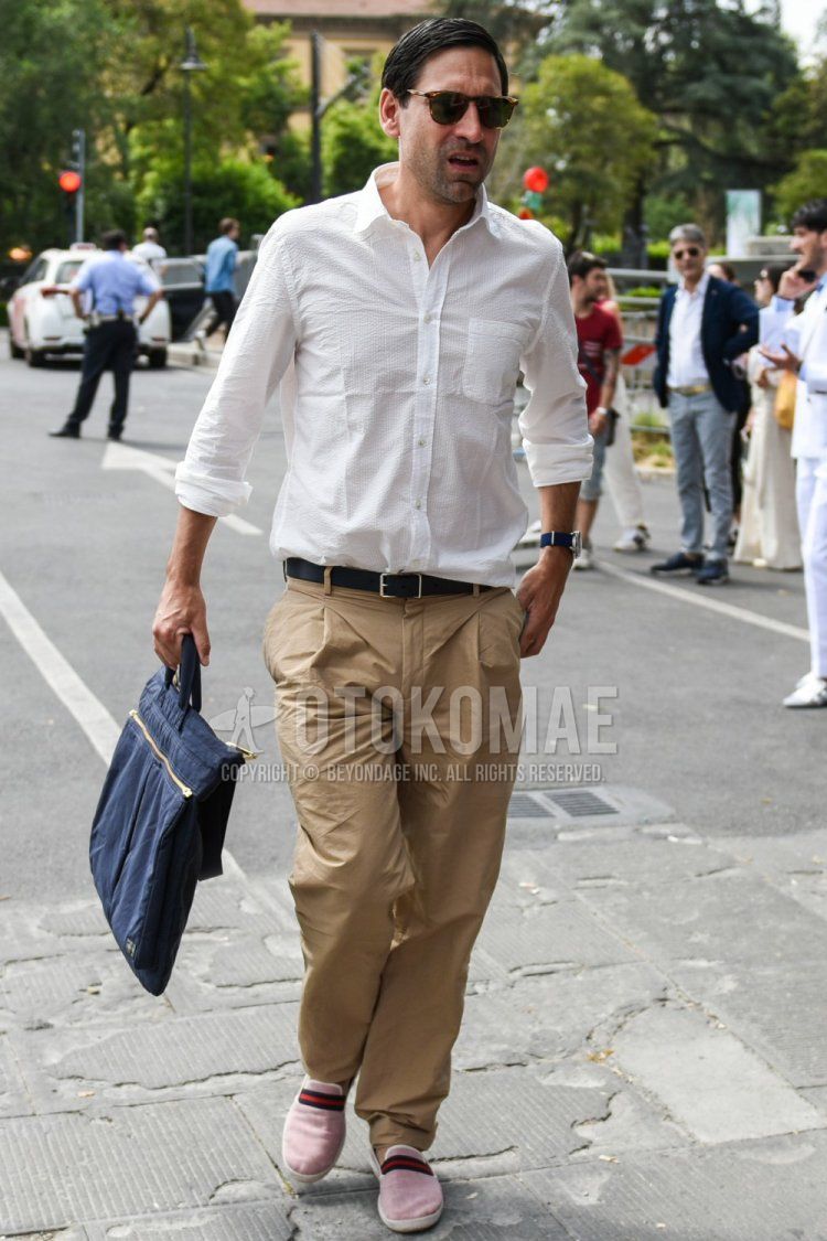 Men's spring/summer coordinate and outfit with brown tortoiseshell sunglasses, plain white shirt, plain black leather belt, plain beige chinos, pink slip-on sneakers, and plain navy briefcase/handbag.