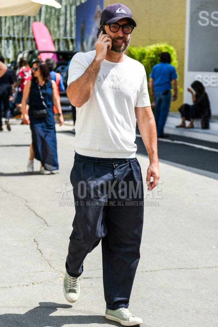 Summer men's coordinate and outfit with a Quiksilver purple solid color baseball cap, white solid color t-shirt, navy solid color wide pants, and green low-cut sneakers.