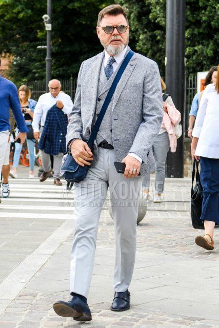 Solid color sunglasses, gray outer tailored jacket, gray top/inner gilet, solid white shirt, solid black leather belt, solid gray slacks, solid black socks, navy monk shoes leather shoes, solid navy shoulder bag, men's spring/summer/fall outfit with Outfit.
