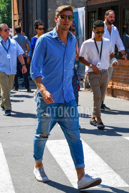 Men's spring and summer coordinate and outfit with brown tortoiseshell sunglasses, blue checked shirt, plain blue damaged jeans, and white low-cut sneakers.