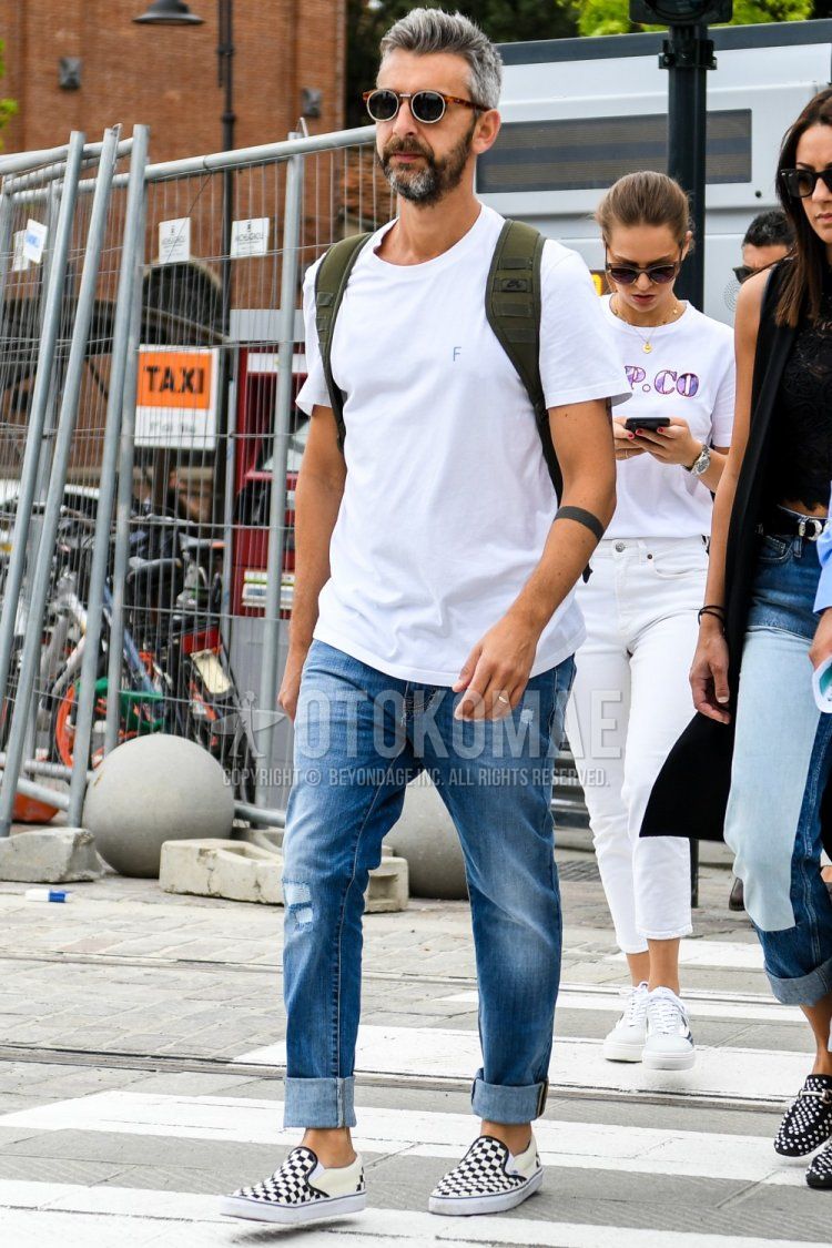 A summer men's coordinate and outfit with tortoiseshell sunglasses, plain white t-shirt, plain blue denim/jeans, and Vans white and black slip-on sneakers.