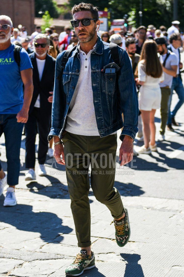 Men's spring and fall coordinate and outfit with plain black sunglasses, plain blue denim jacket from Levi's, plain white polo shirt, plain olive green chinos, and green low-cut sneakers.