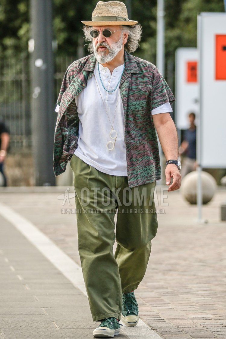 Men's spring/summer outfit with solid beige hat, solid silver sunglasses, olive green camouflage shirt, solid white shirt, solid olive green wide-leg pants, solid olive green pleated pants, and olive green/green sneakers.