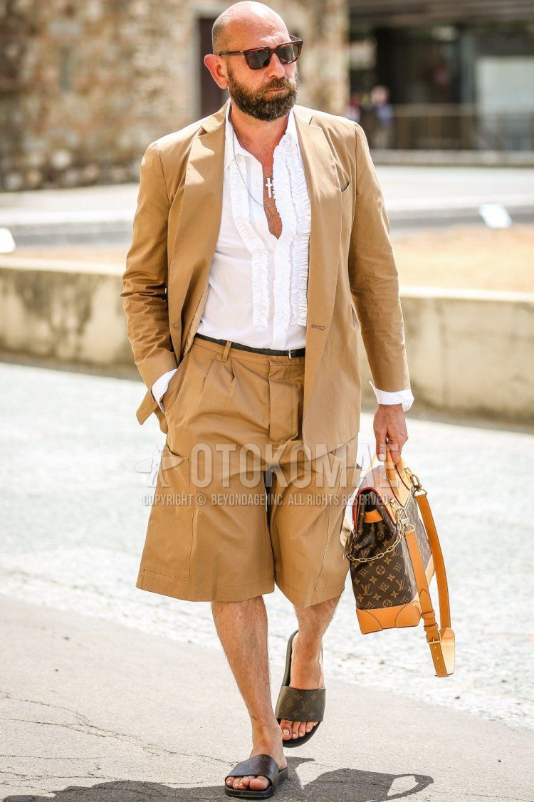 Men's spring/summer outfit and outfit with brown tortoiseshell sunglasses, plain white shirt, plain black leather belt, plain brown shorts, brown leather sandals, brown bag backpack, plain beige/brown casual getup.