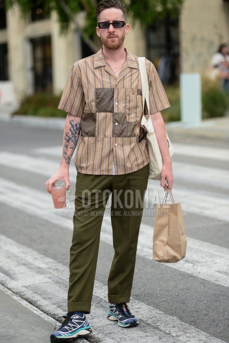 Men's spring and summer coordinate and outfit with plain black sunglasses, beige/brown striped shirt, olive green plain slacks, and light blue/blue sneakers.