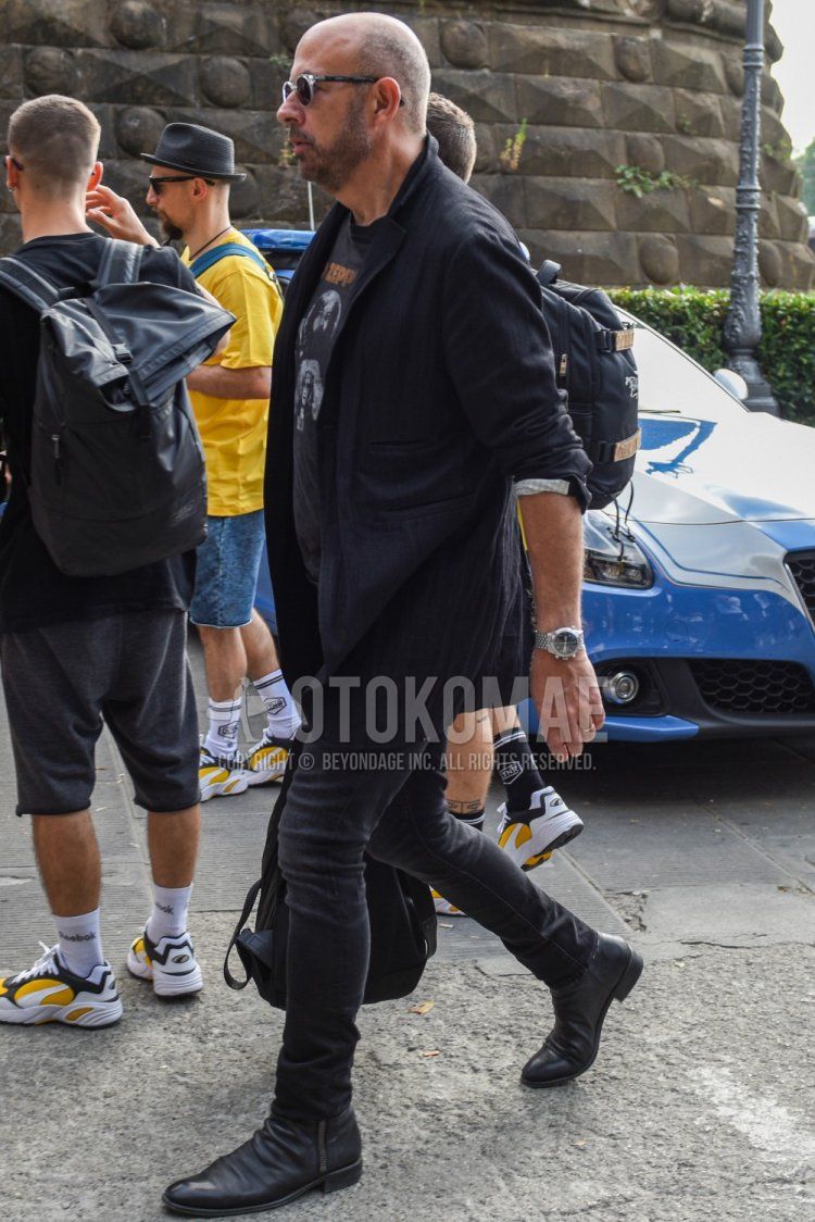 Men's spring/summer/autumn coordination and outfit with clear plain sunglasses, plain black tailored jacket, black graphic t-shirt, dark gray plain denim/jeans, and black boots.