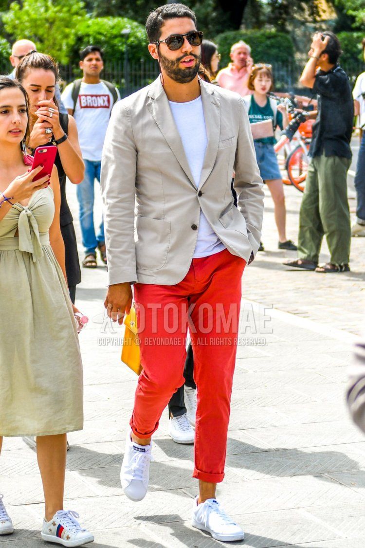 Men's spring/summer coordinate and outfit with brown tortoiseshell sunglasses, plain beige tailored jacket, plain white T-shirt, plain red cotton pants, and white low-cut sneakers.