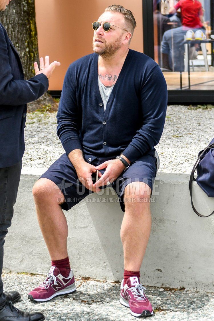 Men's spring, summer, and fall coordinate and outfit with solid color sunglasses, solid color navy cardigan, solid color gray t-shirt, solid color navy shorts, solid color red socks, and red low-cut sneakers by New Balance.