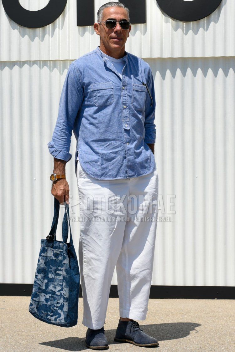 Men's spring/summer outfit and outfit with plain silver sunglasses, plain blue shirt, plain white t-shirt, plain white cotton pants, blue chukka boots, and blue camouflage tote bag.
