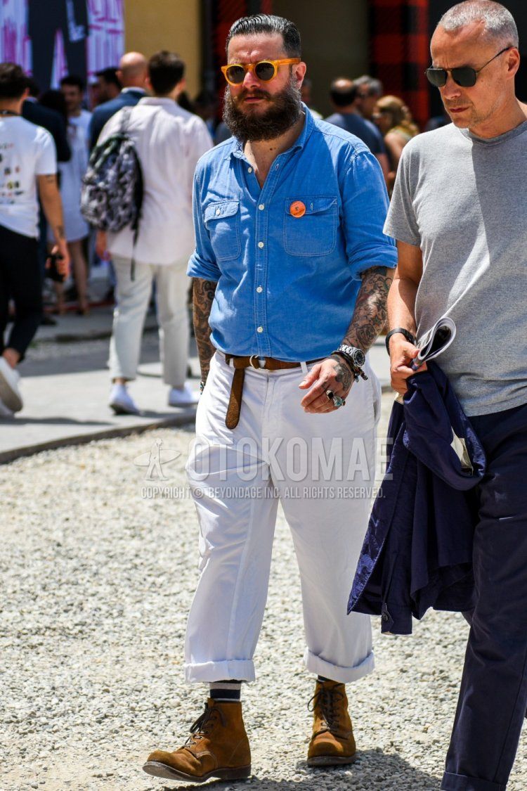 Men's spring/summer/fall outfit with solid orange sunglasses, solid blue denim/chambray shirt, solid brown leather belt, solid white wide-leg pants, multi-colored striped socks, and brown work boots.