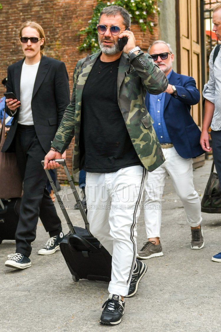 Men's spring, summer, and fall coordinate and outfit with plain sunglasses, olive green camouflage tailored jacket, plain black t-shirt, plain white sidelined pants, and New Balance 574 black low-cut sneakers.