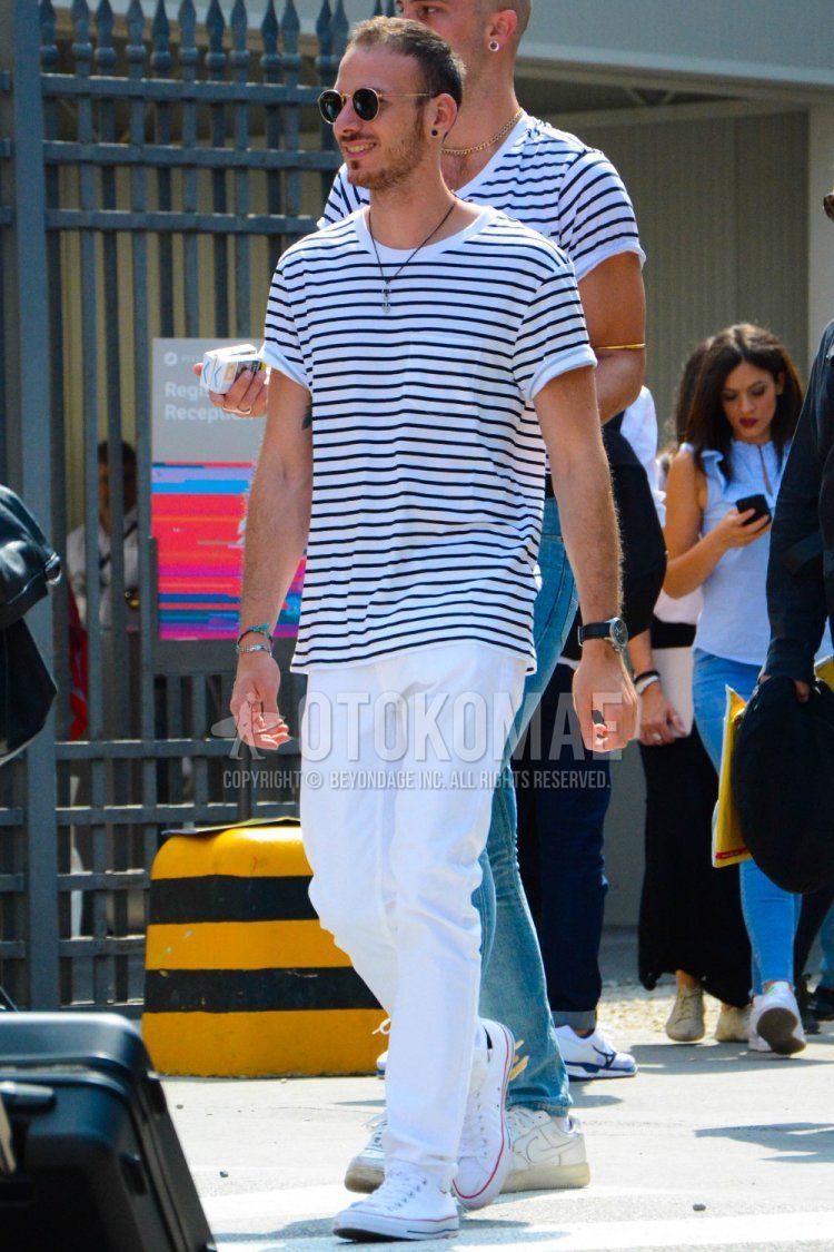 Men's spring/summer coordinate and outfit with round gold plain sunglasses, black/white striped t-shirt, plain white cotton pants, and white low-cut Converse All Star sneakers.