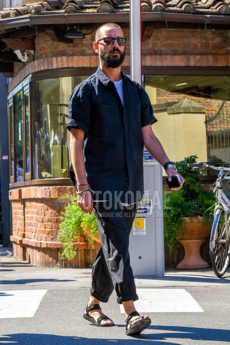 Men's spring/summer coordination and outfit with plain black sunglasses, short-sleeved plain black shirt, plain white t-shirt, plain black jogger pants/ribbed pants, and black sports sandals.