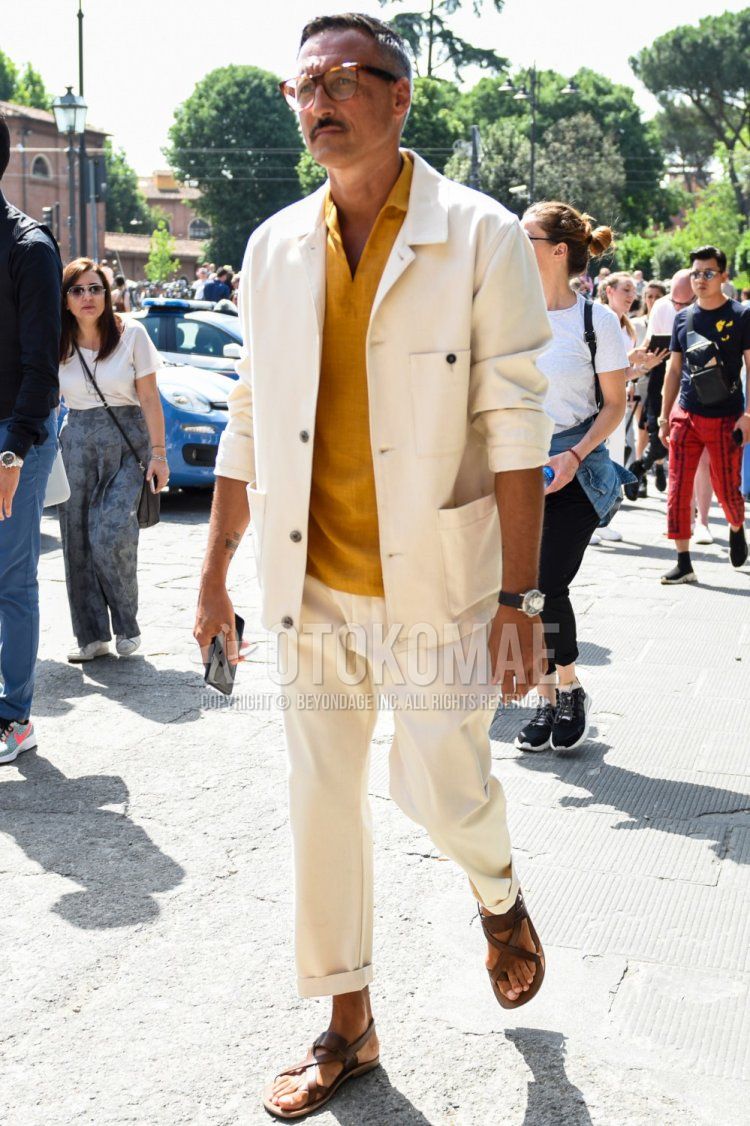 Men's spring, summer, and fall coordinate and outfit with brown tortoiseshell glasses, plain white shirt jacket, plain yellow shirt with linen pullover, plain white cotton pants, and brown leather sandals.