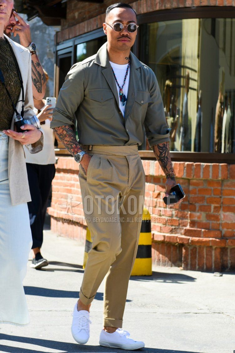 Men's spring, summer, and fall coordinate and outfit with plain black sunglasses, plain olive green/green field jacket/hunting jacket, plain white t-shirt, plain beige beltless pants, and white low-cut sneakers.