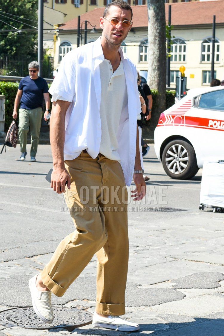 Men's spring/summer coordinate and outfit with plain gold sunglasses, plain beige t-shirt, plain white shirt, plain brown chinos, and white slip-on sneakers.